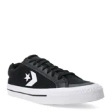 Championes Converse de corte bajo, confeccionados en lona negra con detalles en cuero sintético. Presentan el logo de la marca en el lateral, cierre con cordones y suela de goma blanca con textura.