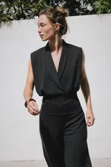 Top sin mangas confeccionado en tejido piqué, con escote cruzado tipo solapa y detalle de pliegues. Presenta una banda ancha ajustada en la cintura y un diseño de hombros caídos.