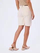 Bermuda de jean color beige, de tiro medio y corte recto, con bolsillos laterales y traseros, y presillas para cinto.