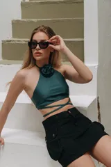 Top de bikini verde oscuro con cuello halter, detalle de flor de tela aplicada en el escote y tiras largas cruzadas para atar alrededor de la cintura.