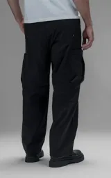 Pantalón cargo de corte regular confeccionado en textil técnico pesado. Presenta cintura elástica con cordón de ajuste, bolsillos laterales en la cintura y bolsillos cargo de gran tamaño en los muslos. Incluye elásticos con tancas en los tobillos para regular la apertura de la pierna.