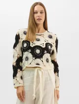 Buzo de tejido crochet con diseño de motivos circulares en contraste blanco y negro, con apliques de pedrería en el centro de los círculos. Presenta corte recto, cuello redondo y manga larga.