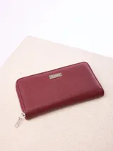 Billetera rectangular de cuero sintético con textura granulada, color bordó. Cuenta con cierre perimetral metálico y placa metálica con el logo de la marca en el frente.