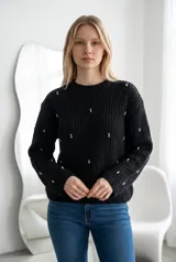 Sweater de punto grueso color negro, con cuello redondo y mangas largas. Presenta un diseño decorado con pequeñas perlas y apliques brillantes distribuidos por toda la prenda.
