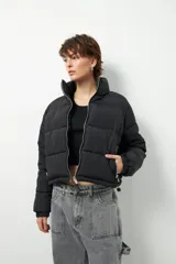 Campera puffer corta negra de nylon, con cuello alto, cierre frontal con cremallera metálica, bolsillos laterales con cierre y cordones ajustables en la cintura.