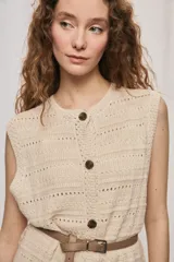 Chaleco de punto color beige, sin mangas, con escote redondo y cierre frontal con botones carey. Presenta diseño calado y silueta amplia.
