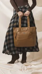 Cartera tipo tote marrón de diseño práctico y versátil, confeccionada en símil cuero con textura granulada. Cuenta con asas cortas fijas, bolsillos exteriores con cierre al frente y atrás, y bolsillos laterales abiertos. Su interior es amplio e incluye bolsillos organizadores. Viene con una correa ajustable y desmontable.