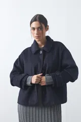 Tapado corto de paño con textura, color marrón, de corte recto y silueta estructurada. Presenta cuello camisero, cierre frontal con botones grandes y mangas largas con detalle de trabas en los puños.