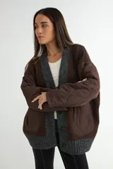 Saco tipo cardigan con diseño híbrido que combina tejido de punto grueso en color marrón y gris con paneles acolchados en color marrón en las mangas y bolsillos frontales. Presenta cierre frontal con botones y cuello en V.