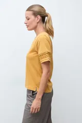 Remera blanca de algodón con cuello en V y mangas cortas que presentan un detalle de puntilla en los bordes.