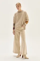 Sweater tejido de lambswool color beige, con cuello redondo y puños acampanados con rayas de colores (marrón, mostaza, bordó y beige). Incluye un detalle de temporada hecho a mano en la espalda.