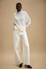 Jersey de punto con textura, color tostado, de cuello subido y manga larga. Presenta un diseño holgado con bajo asimétrico y aberturas laterales.