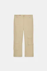 Pantalón de corte recto y largo tobillero, color beige. Presenta tiro medio, trabillas para cinturón, cierre frontal con cremallera y botón, y bolsillos tipo cargo de plastrón en el delantero.