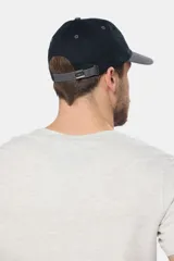 Gorro tipo gorra con visera de lona color azul, con parche tejido frontal que presenta diseño de paisaje y mar.