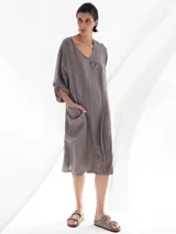 Vestido midi color visón de lino, con cuello en V, mangas 3/4 con botón para sujetar, corte evasé y dos botones decorativos en el frente.