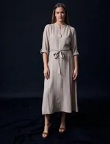 Vestido maxi color beige, con cuello mao y escote en V. Presenta mangas largas con presilla y botón para regular el largo, y un lazo ajustable en la cintura que marca la silueta.