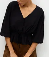 Blusa peplum de viscosa negra con escote en V cruzado, mangas cortas abullonadas con elástico en los puños y cordón ajustable en la cintura.