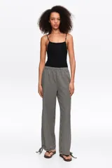 Pantalón de corte recto y tiro medio, con estampa de cuadros en blanco y negro. Posee cintura elástica y detalles de lazos ajustables en los tobillos.