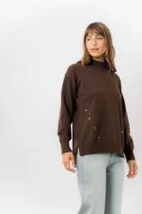 Sweater de tejido de punto color marrón, con cuello alto, corte relajado y terminaciones en rib en puños y cintura. Presenta una hilera de botones metálicos decorativos en uno de los laterales.