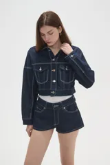 Campera de jean de corte cropped, color azul oscuro con costuras en contraste. Presenta cuello clásico, cierre frontal con botones metálicos y bolsillos frontales con solapa.