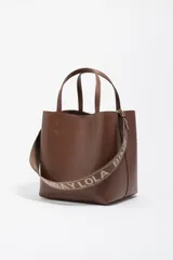 Bolso de mano tipo tote de Bimba y Lola, color marrón, confeccionado en piel reconstituida. Presenta doble asa de mano, asa de tejido ajustable con logo de la marca, cierre de botón de presión y logo metálico frontal.