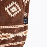 Buzo polar marrón con estampado geométrico en tonos beige y blanco, cuello alto con cierre de botones a presión, bolsillo tipo canguro y bolsillo en el pecho con cierre. Marca Merrell.