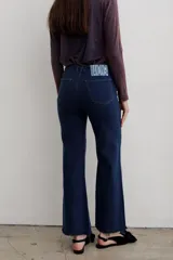 Jean de denim azul de tiro medio, con corte flare y costuras frontales destacadas.