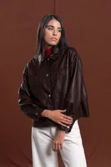 Chaqueta de cuero sintético color marrón, con diseño de corte recto, cuello camisero, cierre frontal con botones metálicos y bolsillos frontales tipo parche.