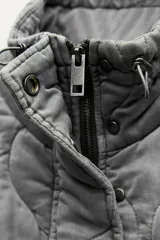 Chaleco gris acolchado con cuello alto, cierre frontal con cremallera metálica, bolsillos de plastrón en delantero y bajo ajustable con cordones.