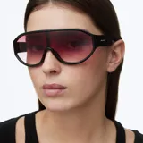 Lentes de sol estilo deportivo con lente panorámica envolvente de color rosado degradado y montura negra de diseño técnico.