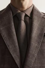Blazer regular fit de Zara, confeccionada en tejido de lino y lana con diseño a cuadros en tonos marrones y grises. Cuenta con solapas de muesca, cierre frontal de un botón y bolsillos con solapa en la cadera.