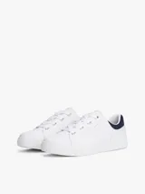 Zapatillas de tenis minimalistas Tommy Hilfiger, confeccionadas en piel napa blanca con suela gruesa tipo cupsole. Presentan un diseño de corte bajo con cordones, detalle de panel azul marino en el talón y logo metálico de la marca en el lateral.