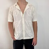 Camisa de tejido de punto calado color negro, con cuello solapa, cierre frontal de botones y mangas cortas.