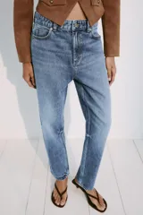 Jeans mom fit de tiro alto confeccionados en denim azul claro, con diseño de cinco bolsillos, trabillas para cinturón y cierre frontal con cremallera y botón metálico.