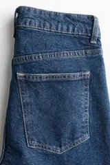 Jean de tiro alto con corte mom slim, confeccionado en denim azul oscuro con leve elasticidad. Presenta diseño de cinco bolsillos, cierre con botón y pierna recta que se estrecha ligeramente hacia el bajo.