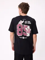 Remera negra de corte holgado con estampa gráfica en la espalda que incluye el número 85, personajes animados y la frase 'Play hard, surf harder'.