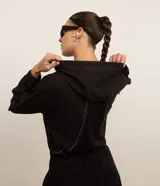 Campera deportiva cropped color negro, con capucha y mangas largas. Presenta cierre frontal, detalle reflectante y está confeccionada en tejido tecnológico.