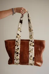 Cartera grande de cuero color marrón con asas de cuero con estampado animal print y ojales dorados.