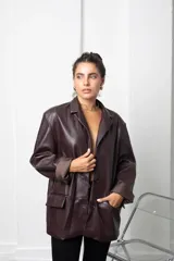 Blazer de eco cuero color bordó, con diseño oversize, hombreras estructuradas y solapas clásicas. Presenta mangas largas con puños vueltos y cierre frontal con botón.