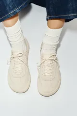 Zapatillas tipo deportiva Barefoot confeccionadas en serraje de color beige, con diseño de puntera amplia y suela flexible. Cuentan con detalles de pespuntes, cordones al tono y refuerzo en contraste en la parte trasera.