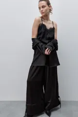 Pantalón de pierna amplia y calce holgado, color negro, confeccionado en tejido satinado. Cuenta con cintura elastizada, recortes horizontales y tiras regulables en los ruedos.