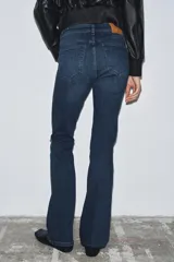 Jeans de tiro medio con corte bootcut y ajuste slim. Presenta diseño de cinco bolsillos, trabillas en la cintura y cierre frontal con cremallera y botón. Incluye detalle de pespuntes marcados a contraste.