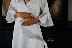 Bata corta de satén elastizado color blanco, con mangas tres cuartos terminadas en volados y lazo ajustable en la cintura.