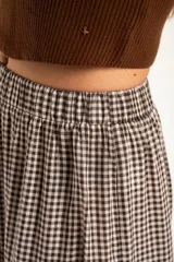 Falda larga de corte evasé con diseño de cuadros vichy en tonos marrón y blanco. Presenta una cintura elástica y un diseño de tres volados horizontales que aportan volumen y movimiento.