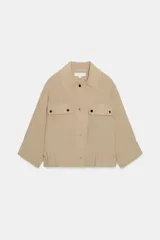 Chaqueta corta color beige con cuello solapa y cierre frontal de botones. Cuenta con mangas con vuelta, bolsillos de parche con solapa en el pecho y bajo ajustable.