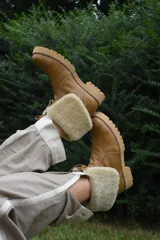 Botas de cuero color tostado con caña baja y vuelta de corderito sintético, suela track de goma y cordones frontales.