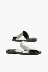 Sandalias planas de cuero color blanco hueso, con dos tiras anchas cruzadas en la parte superior y diseño minimalista.