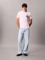 Remera rosada de manga corta con cuello redondo y corte regular, confeccionada en algodón regenerativo. Cuenta con un estampado gráfico en caja de color celeste con el monograma "ck" en negro en el pecho.