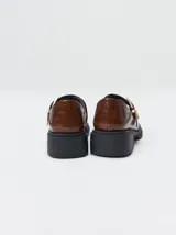 Zapatos tipo guillermina Mutma modelo Punko, color marrón, confeccionados en cuero. Presentan punta cuadrada, detalle texturizado en la parte delantera, tira en el empeine con hebilla metálica dorada y suela chunky de goma negra con taco bajo.