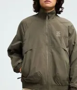 Campera rompeviento color verde militar, con cierre frontal de cremallera, cuello alto, puños y cintura elásticos. Presenta recortes delanteros y un pequeño logo estampado en el pecho.